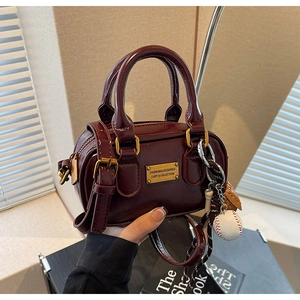 Detail of burgundy mini Boston bag with golden logo plaque and baseball charm
