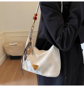 Detail of white hobo bag featuring amber bead strap and gold logo with vintage charms