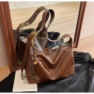 Detail view of brown vintage leather tote with adjustable strap and gold bell charm
