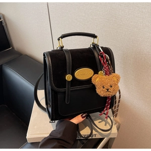 Close-up of black leather bag featuring a gold metal brand plate and cute bear charm