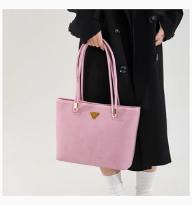 Detail of pink matte tote bag with gold triangle hardware carried with a black trench coat