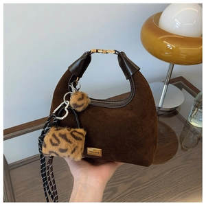 Detail of dark brown suede dumpling bag with leopard print fur pom-poms and metal heart charm