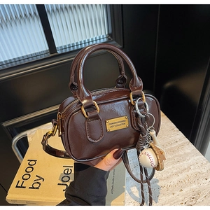 Detail of dark brown leather mini pillow bag with golden logo and baseball charm