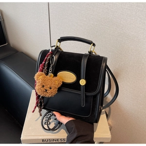 Detail of black crossbody bag featuring textured leather and cute teddy bear charm