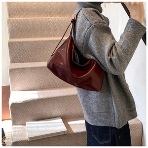 Close-up of a burgundy glossy leather tote bag styled with a gray sweater for autumn