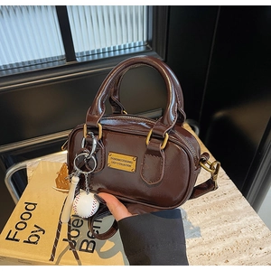 Detail of a chocolate patent leather mini Boston bag with gold plate and sporty charm