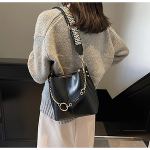 Détail du sac seau en cuir noir avec bandoulière jacquard et accessoires en chaîne dorée