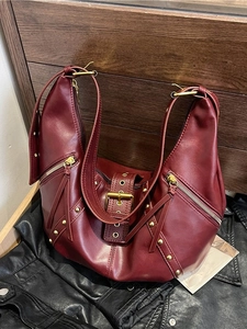 Retro burgundy crescent bag with silver rivets and zippers on a dark leather background