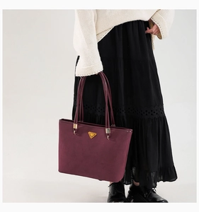 Detail of burgundy tote bag with gold logo on suede leather held by a model