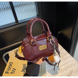 Detail of burgundy mini pillow bag featuring glossy finish and sports charms