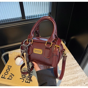 Detail of burgundy Boston bag showing glossy finish, gold metal plaque and baseball charm