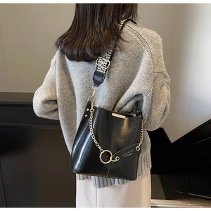 Détail du sac seau en cuir noir avec large bandoulière tissée et chaîne dorée