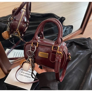 Detail of burgundy Boston bag with baseball charms and polished metal nameplate