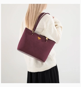 Detail of burgundy suede tote bag featuring a gold triangular logo on a white sweater