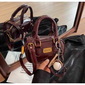 Close-up of deep red Boston bag featuring glossy PU leather and a baseball charm