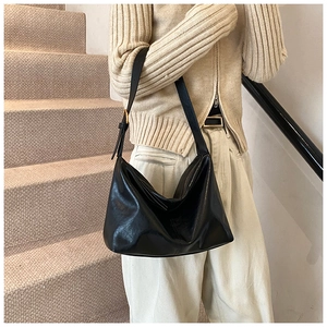 Detail of black glossy leather hobo bag with gold hardware on person on stairs