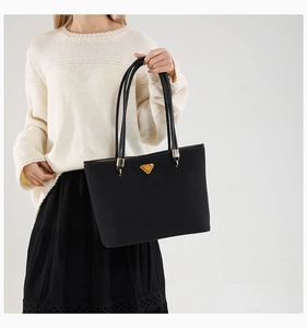Detail of black tote bag with gold triangle buckle and long leather handles worn by model