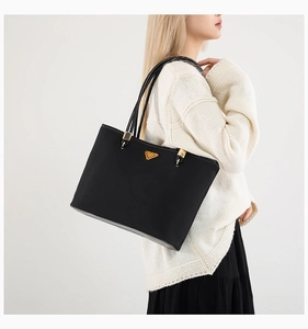 Detail of a large black tote bag with gold triangular logo and slim shoulder straps
