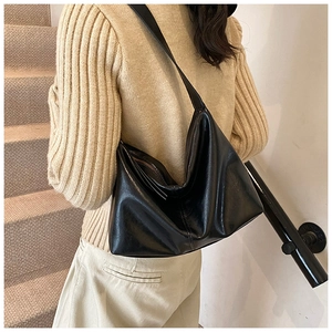 Detailed view of a black glossy faux leather tote bag worn over a beige sweater