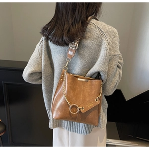 Détail du sac seau en cuir marron vintage avec chaîne dorée et bandoulière tissée