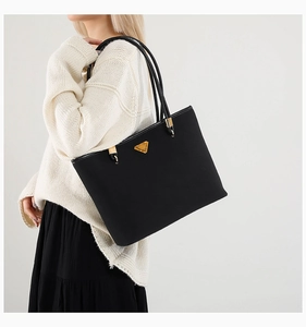 Detailed view of the black leather tote bag featuring a golden triangle logo on the front