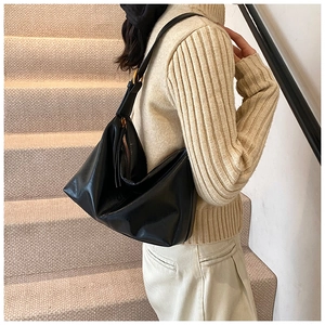 Detail of a black leather hobo bag with gold hardware worn over a beige sweater