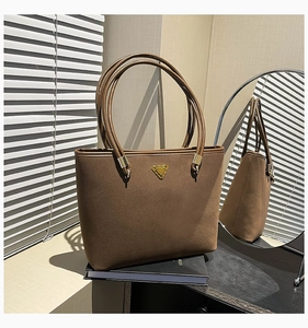 Detail of a brown suede tote bag featuring a golden triangle buckle and long shoulder straps