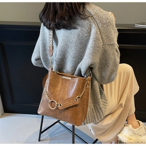 Détail du sac seau en cuir marron avec bandoulière tissée et chaîne dorée