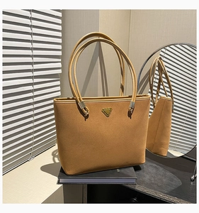 Macro detail of tan suede tote bag with metal triangle plaque and sleek long handles