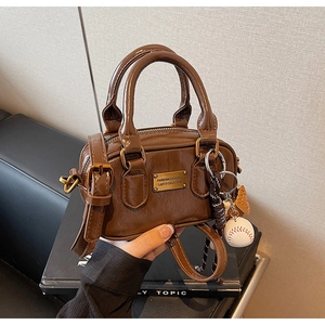 Detailed macro view of brown patent leather bag with gold hardware and baseball charm