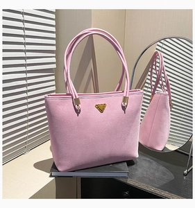 Detail of pink suede tote bag with golden triangle plaque on a black surface