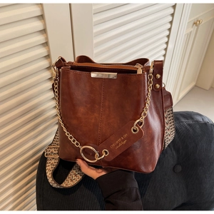 Détail du sac seau marron montrant la bandoulière à motifs et la chaîne dorée