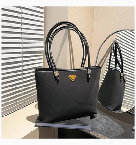 Detail of black tote bag with matte leather texture and golden triangular metal logo