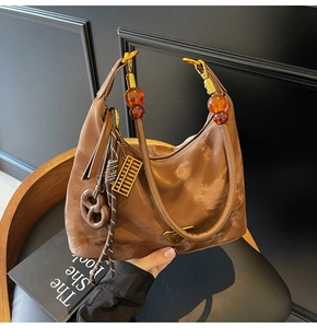 Detail of brown suede hobo bag with acrylic beads, golden charms, and metal logo plaque