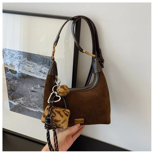 Detail of dark brown suede dumpling bag with golden metal plate and leopard plush charm