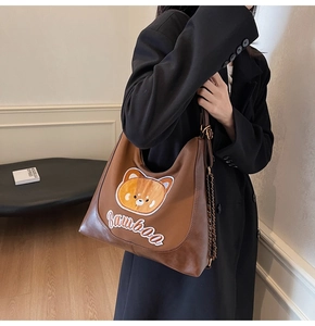 Détail du sac hobo marron avec broderie ours, texte de marque et bandoulière chaîne