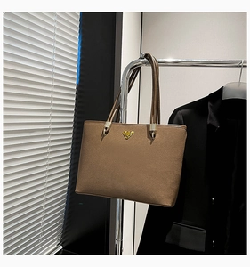 Detail of high-quality brown suede tote bag featuring a golden triangular metal logo