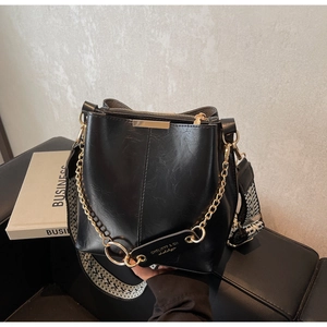 Détail du sac seau noir avec chaîne dorée et bandoulière géométrique sur canapé en cuir