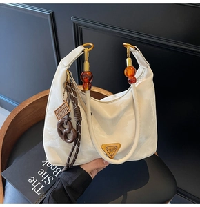 Macro detail of creamy white hobo bag with unique amber bead handle and gold metal emblem