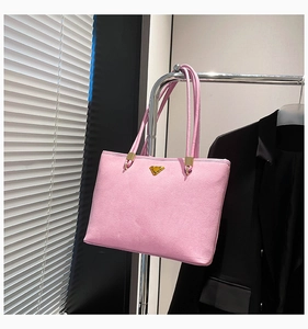 Close-up of pink suede tote bag featuring a triangle metal logo on a minimalist hanger