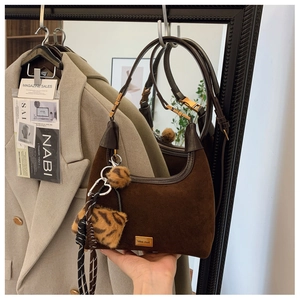 Detail of a brown suede hobo bag with dark leather trim and leopard print charm