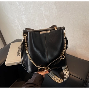 Détail du sac seau en cuir noir avec chaîne dorée et bandoulière tissée géométrique