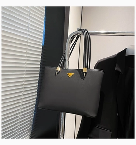Detail of black tote bag featuring gold triangle plaque and metallic strap hardware