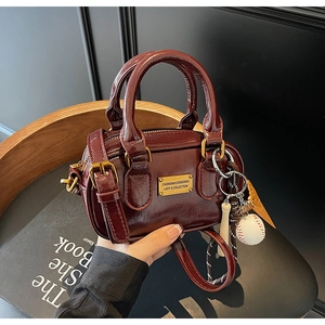 Detail of burgundy leather handbag featuring golden hardware and a baseball charm
