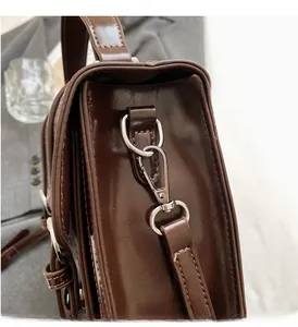 Detailed close-up of dark brown leather satchel with silver metal D-ring and lobster clasp