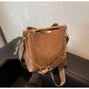 Détail du sac seau en cuir marron avec bandoulière géométrique et chaîne dorée