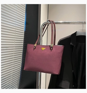 Detailed view of burgundy suede tote bag with golden triangle hardware on a metal hanger
