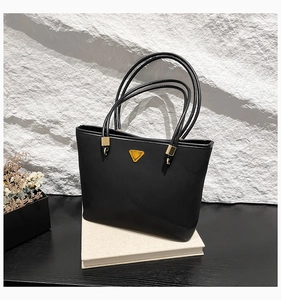 Detail of black matte tote bag with triangular gold logo plaque and leather texture