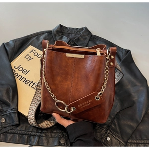 Détail du sac seau marron en cuir avec bandoulière tissée et chaîne dorée
