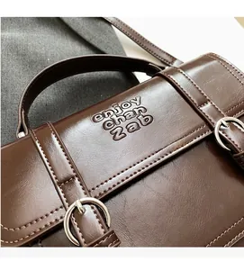 Detail of brown vintage PU leather handbag featuring dual silver buckles and embossed text